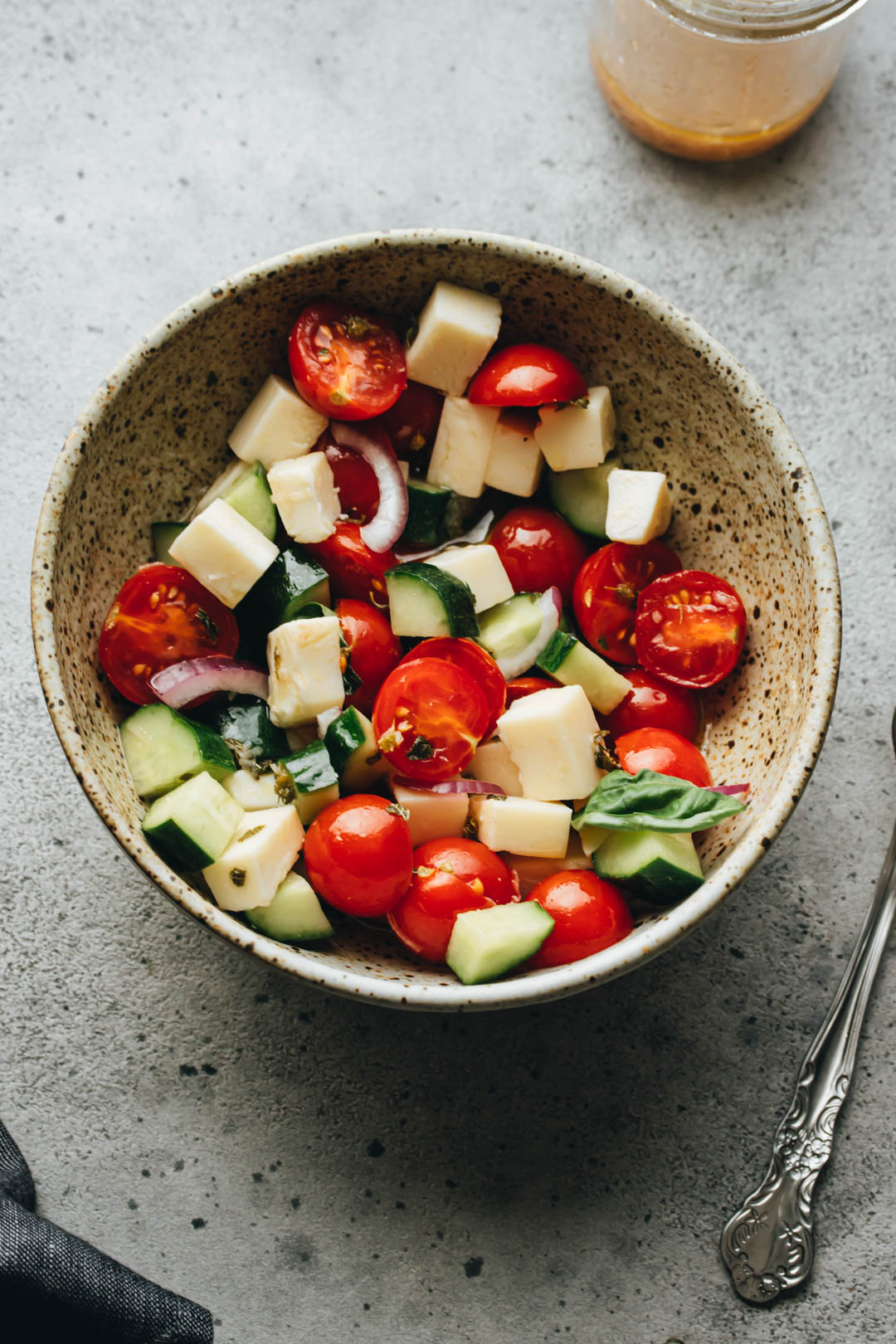 Italian Tomato and Cucumber salad in a white bowl with a dressing jar, napkin, and fork on the side