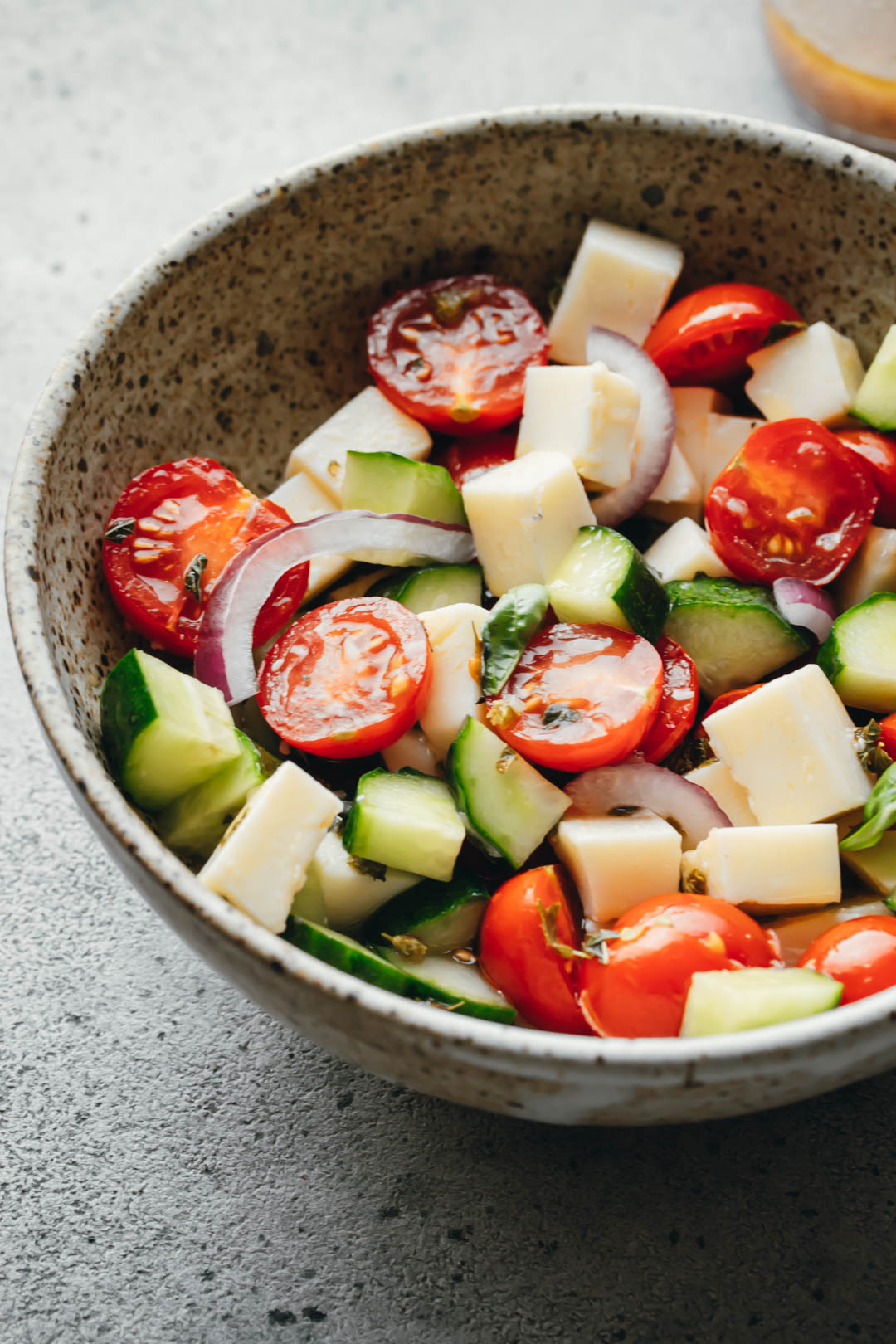 Italian Tomato and Cucumber salad in a white bowl with a dressing jar on the side