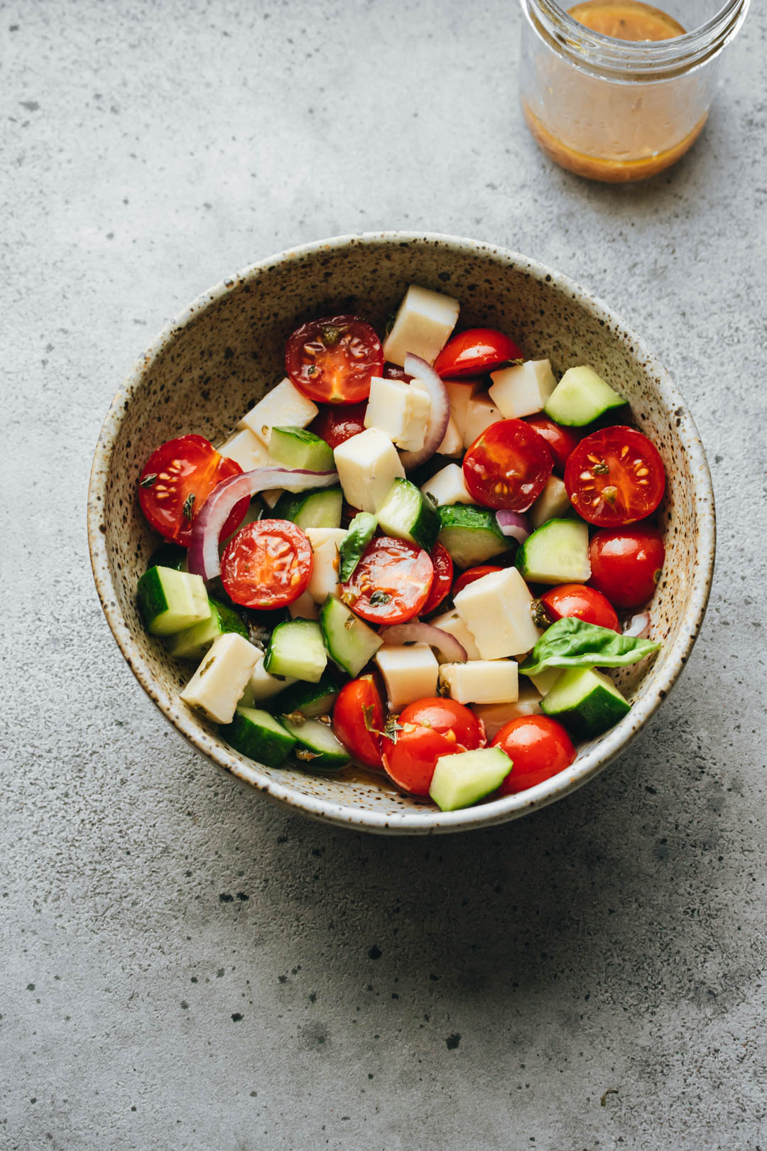 Italian Tomato and Cucumber salad in a white bowl with a dressing jar on the side