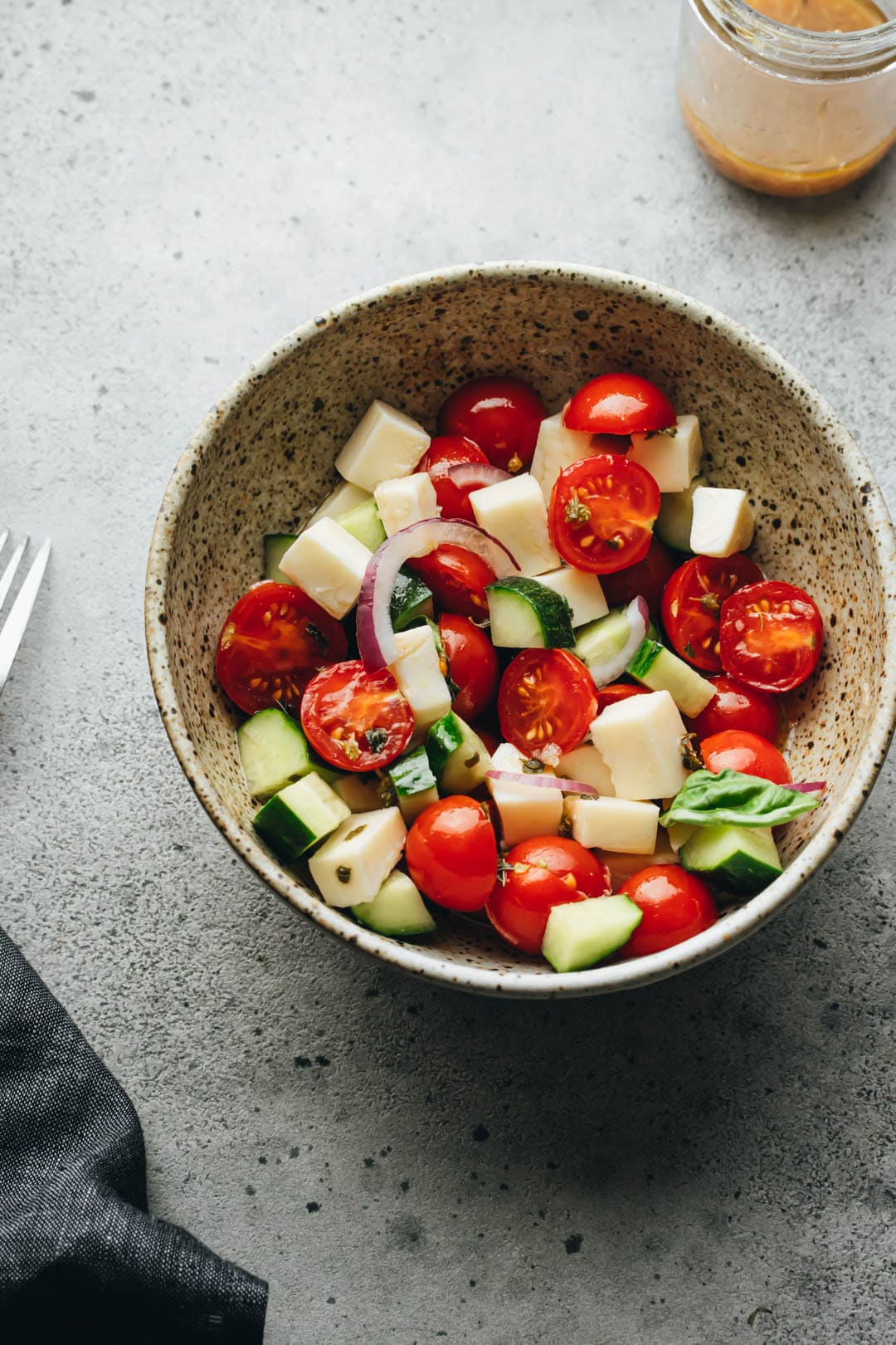 Italian Tomato and Cucumber salad in a white bowl with a dressing jar, napkin, and fork on the side