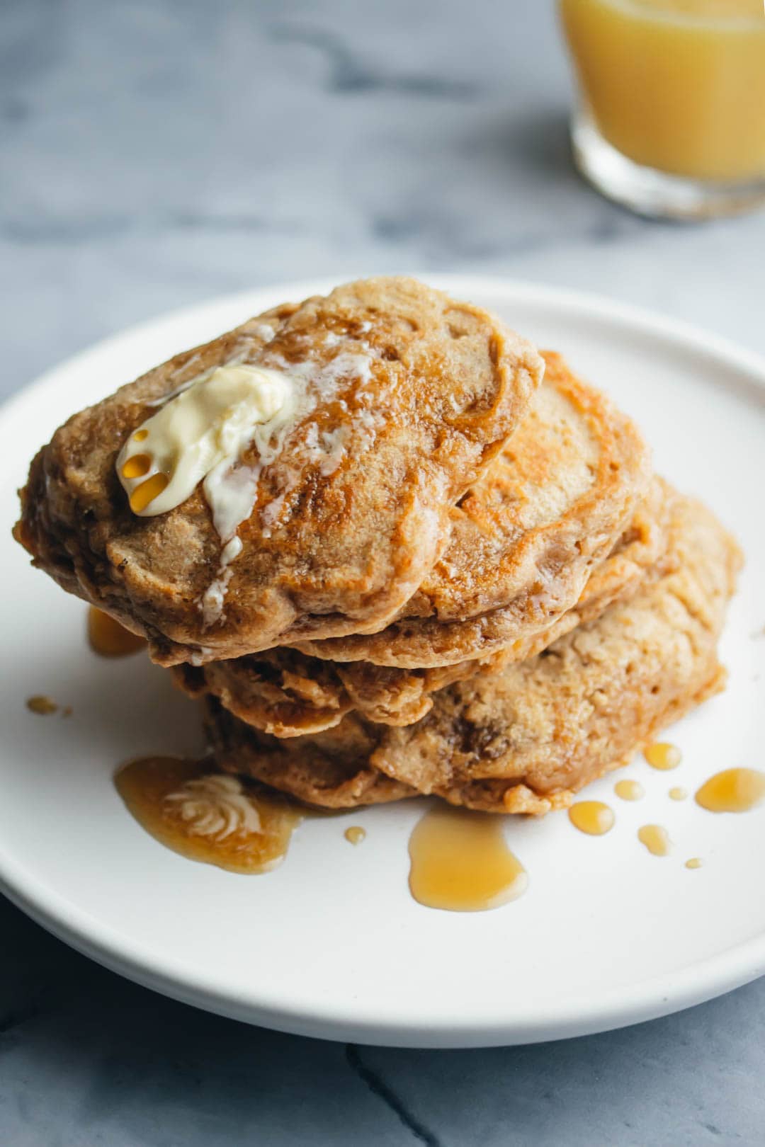 a stack of buttermilk pancakes for two topped with butter and maple syrup and a glass of orange juice on the side