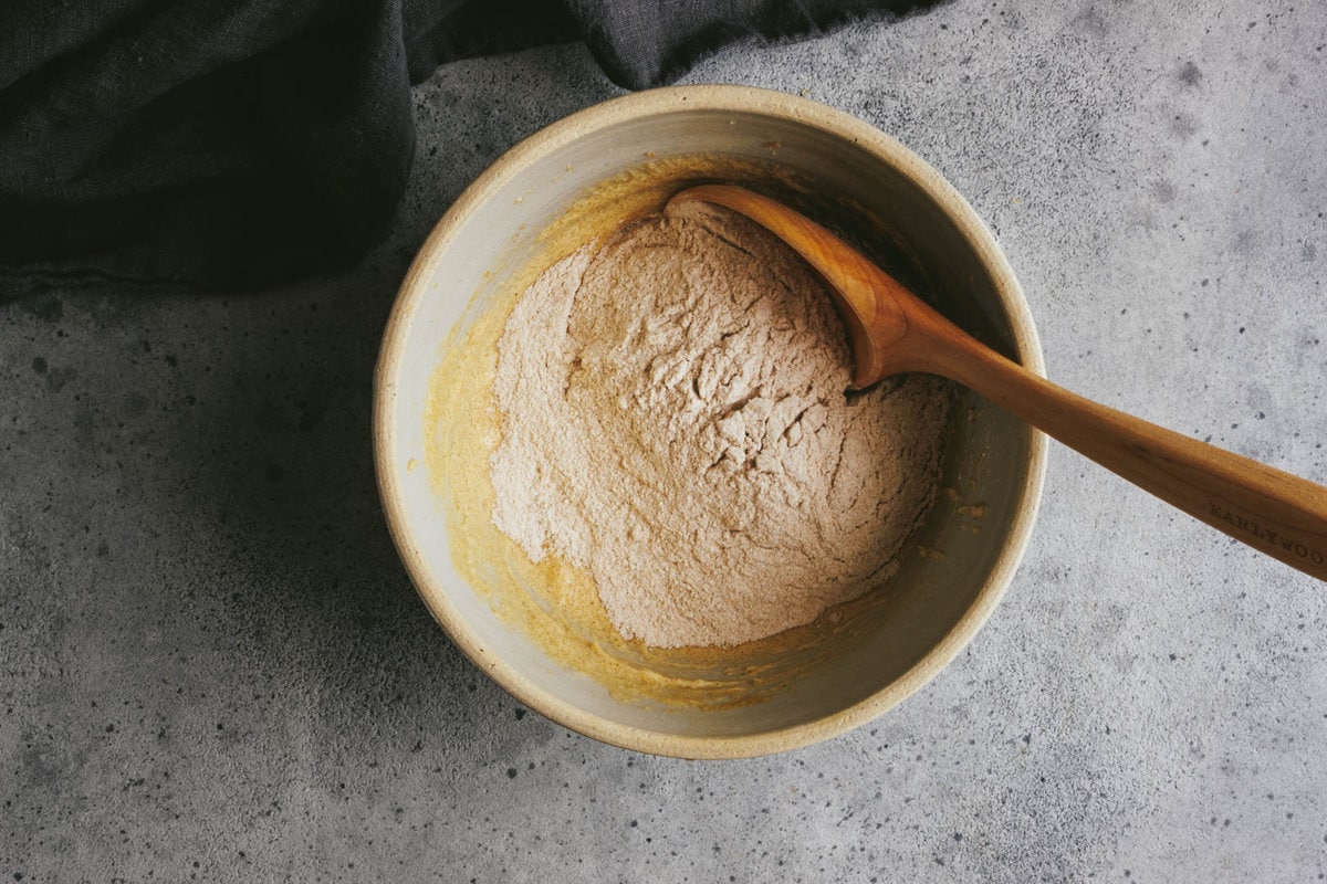 in a large bowl, flour is folded into the wet ingredients with a wooden spoon