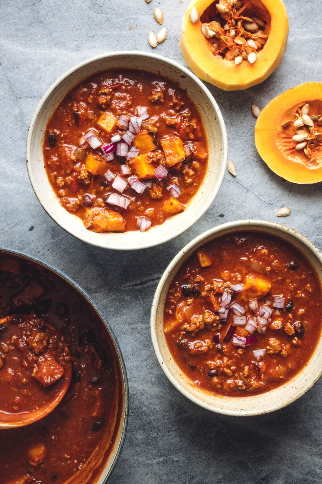 Two bowls filled with roasted Butternut Squash Beef chili with butternut squash and a pot of butternut squash chili on the side