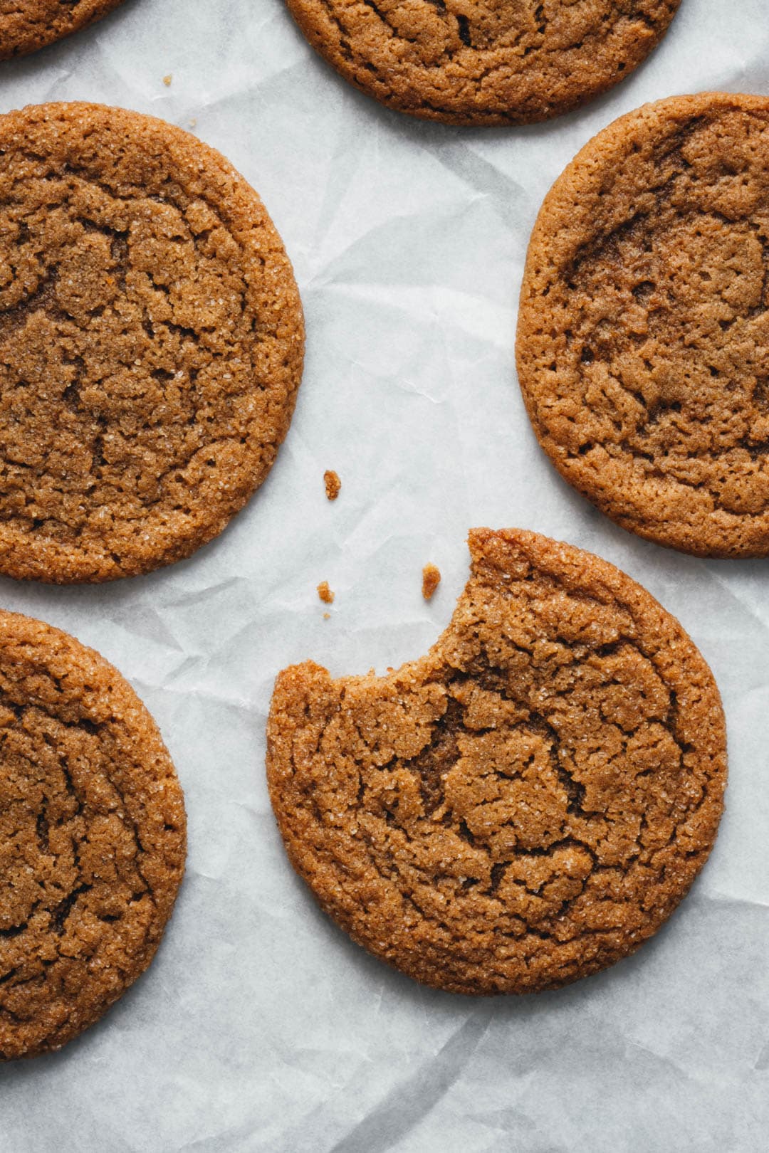 thin and chewy ginger molasses cookies with a bite taken out of one on parchment paper