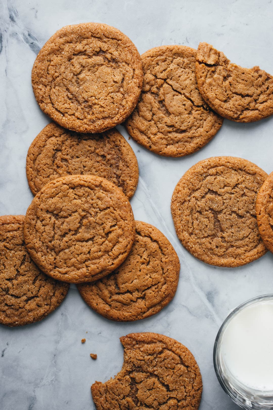 thin and chewy ginger molasses cookies with a bite taken out of one and a glass of milk on the side