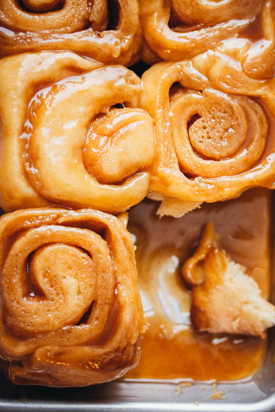 3 small batch sticky buns in a pan with a bun piece swirled in caramel